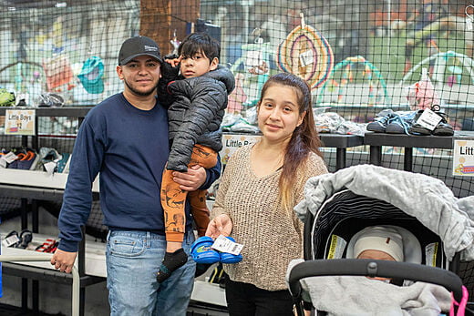 Mom pushing a stroller with a baby, who is covered with a blanket. Dad is holding a toddler boy.