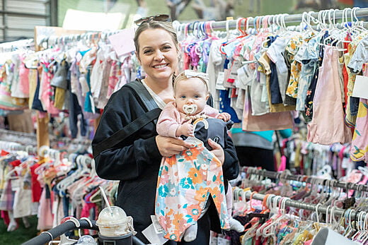 Mom holding baby while standing in the middle of an aisle of girl's clothing