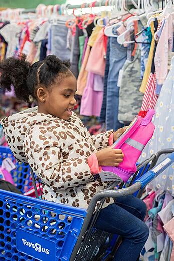 Young girl is sitting in a blue shopping cart looking at an item.