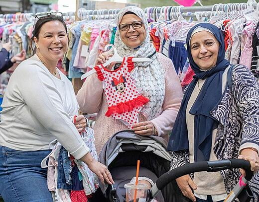 3 women stop and smile while shopping. One is holding up a bathing suit